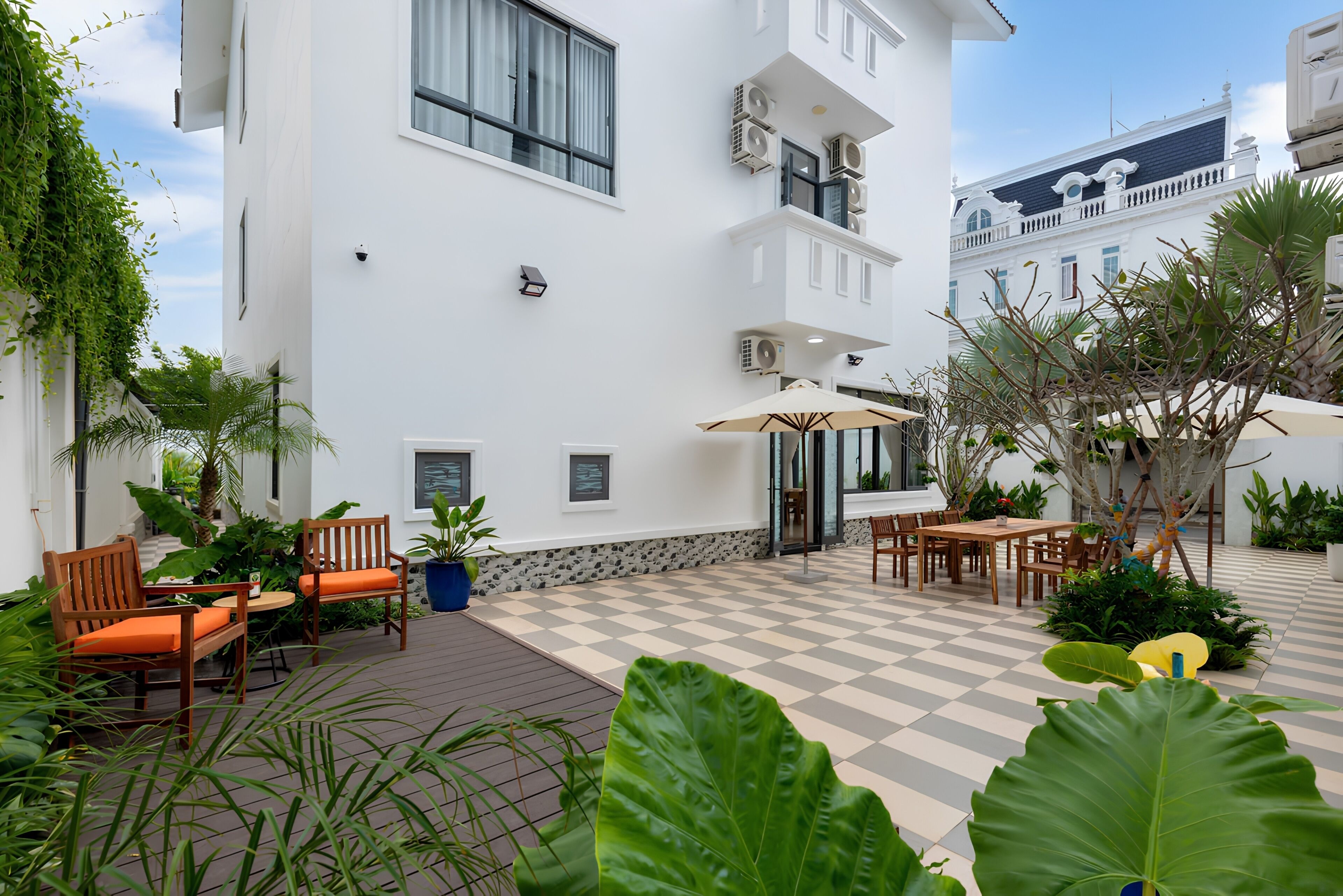 A courtyard with outdoor seating, a checkered floor, and a white building with multiple air conditioning units.