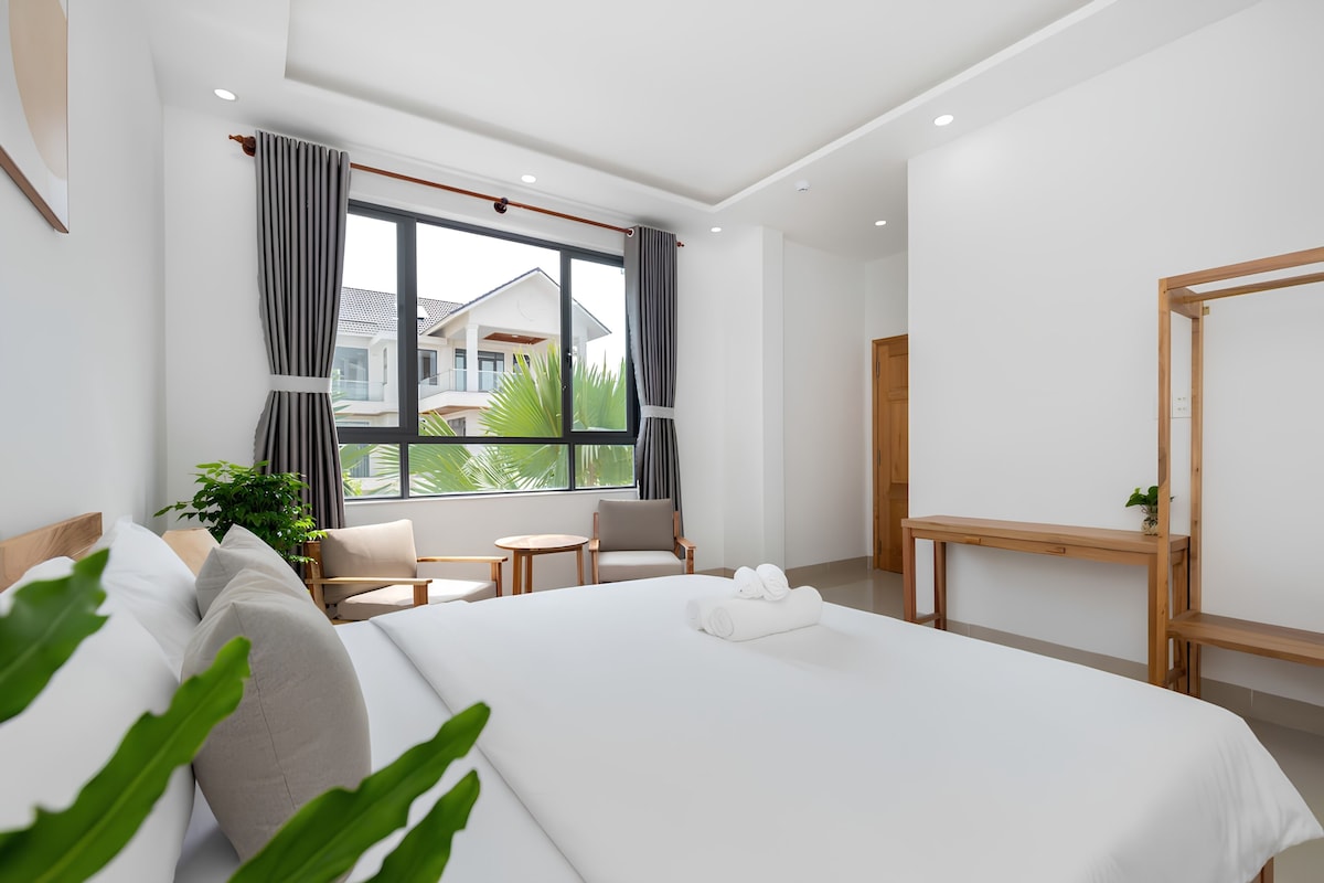Ett modernt hotellrum med en stor säng, en sittgrupp med ett bord och utsikt över ett hus genom fönstret.