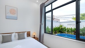 A hotel room with a large bed, a bedside lamp, a view of a swimming pool, and a framed picture on the wall. - Luxury An Home Beach Villa (Rach Dua)