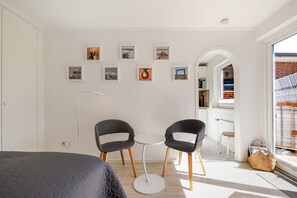 Ein modernes Zimmer mit einem Bett, zwei Stühlen, einem kleinen Tisch und einem Bücherregal.