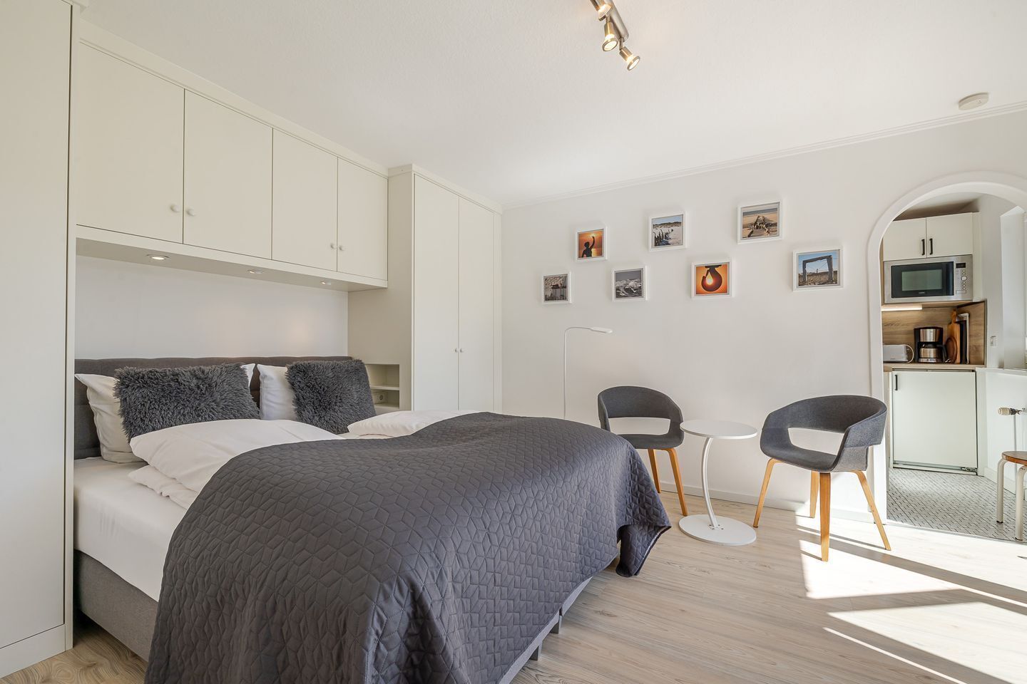 Un dormitorio moderno con una cama, dos sillas, una mesita y una kitchenette.