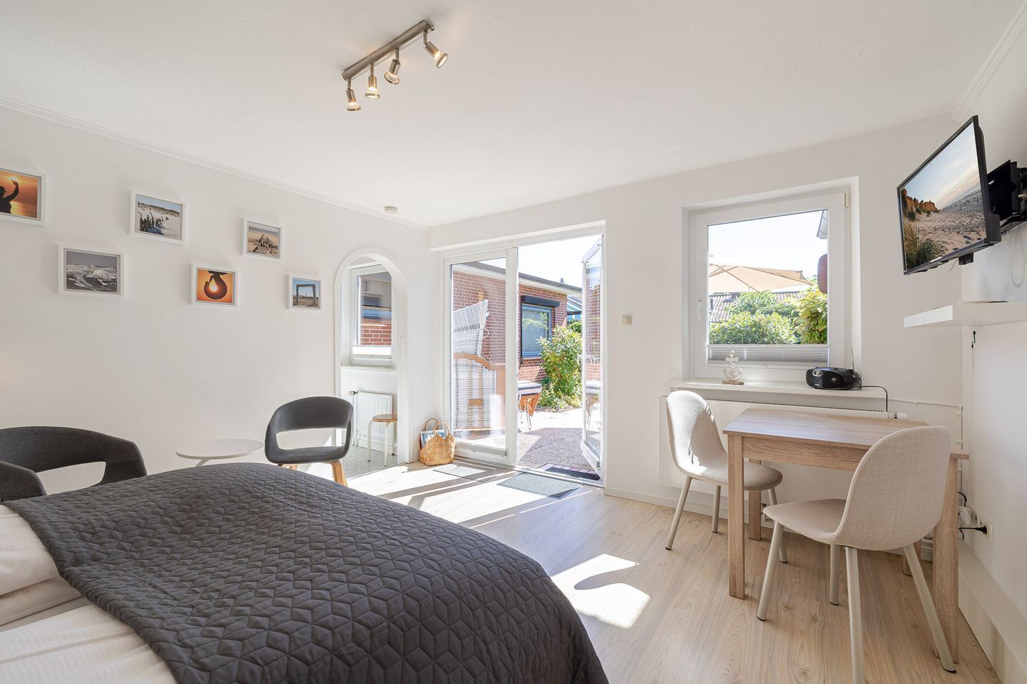 A modern bedroom with a bed, a desk, and a chair, a large window, and artwork on the walls.