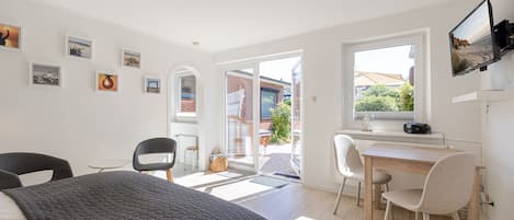 A modern bedroom with a bed, a desk, and a chair, a large window, and artwork on the walls.