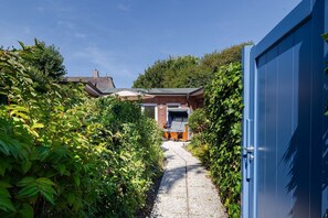 Ein Weg führt zu einem Ziegelhaus mit einer überdachten Sitzgruppe im Freien.