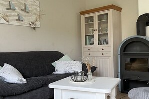 Ein Wohnzimmer mit einem dunkelgrauen Sofa, einem weißen Beistelltisch, einer Vitrine und einem schwarzen Kamin.