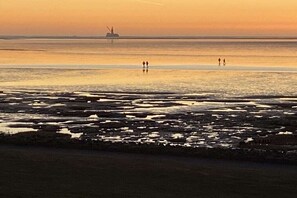 A beach scene with a calm sea, a distant ship, and two people walking. - Holiday home in the North Sea with 3 bedrooms (Friedrichskoog-Spitze)
