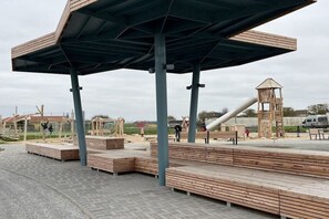 A playground with wooden benches, a climbing structure, and a slide. - Holiday home in the North Sea with 3 bedrooms (Friedrichskoog-Spitze)