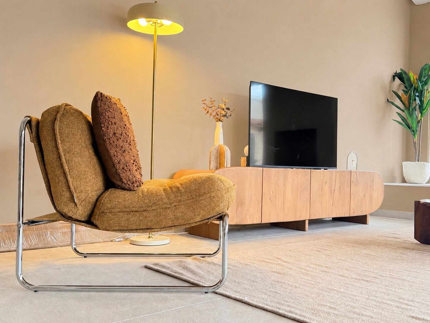 A modern living room with a sofa, a television, a floor lamp, and a potted plant.