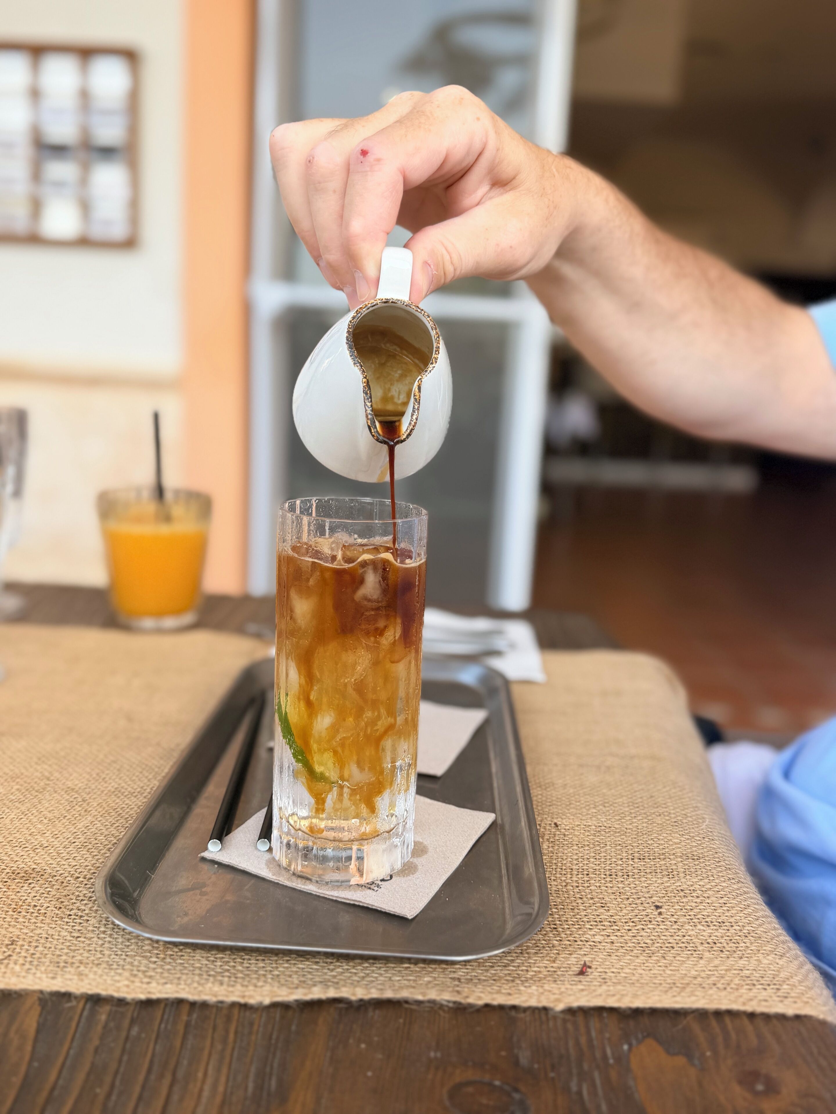 A hand pouring a dark liquid into a tall glass with ice cubes.