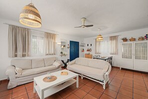 A living room with two sofas, a coffee table, a ceiling fan, and a dining area with chairs and a table.