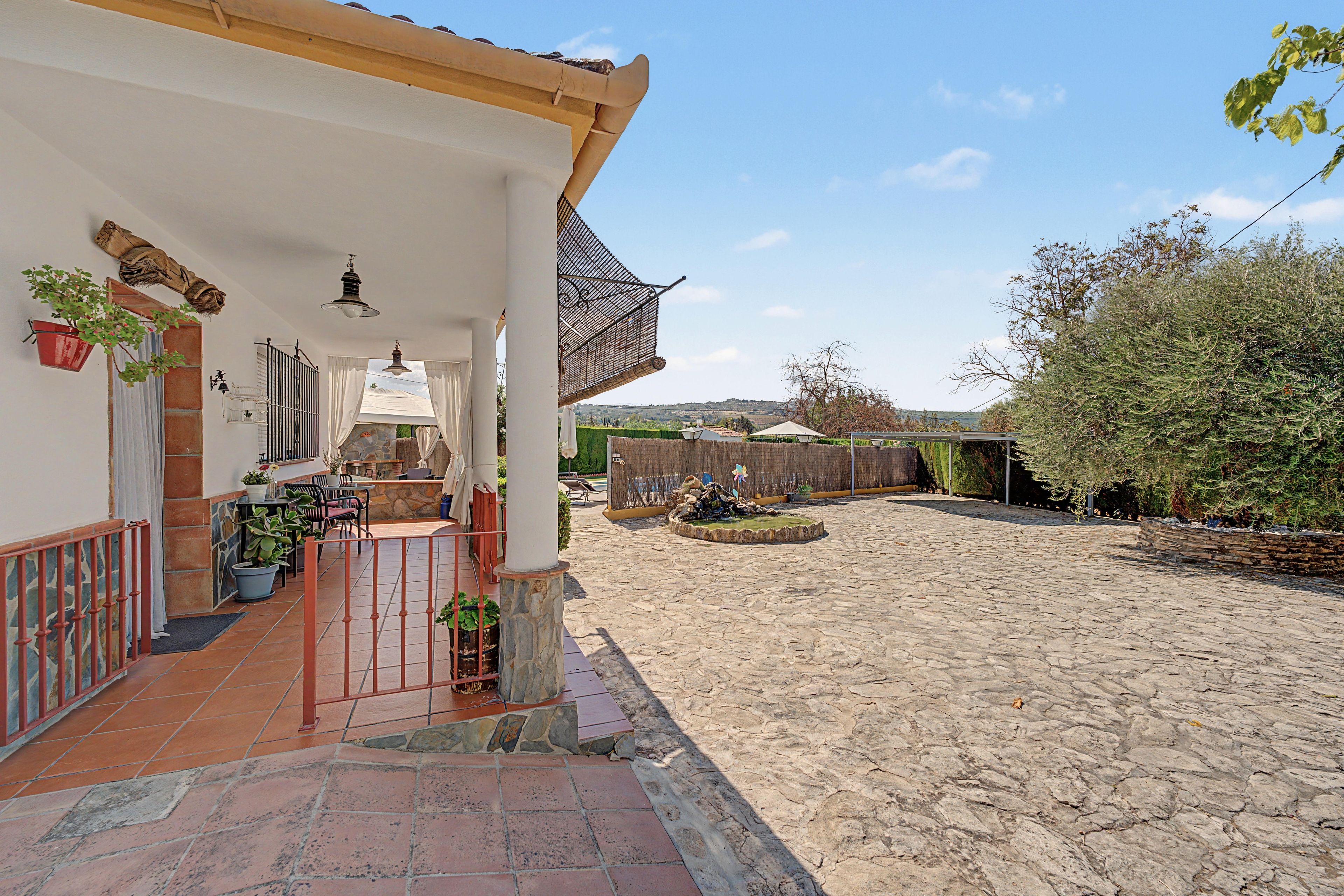Un patio cubierto con piso de piedra, mobiliario exterior y vistas del paisaje circundante.