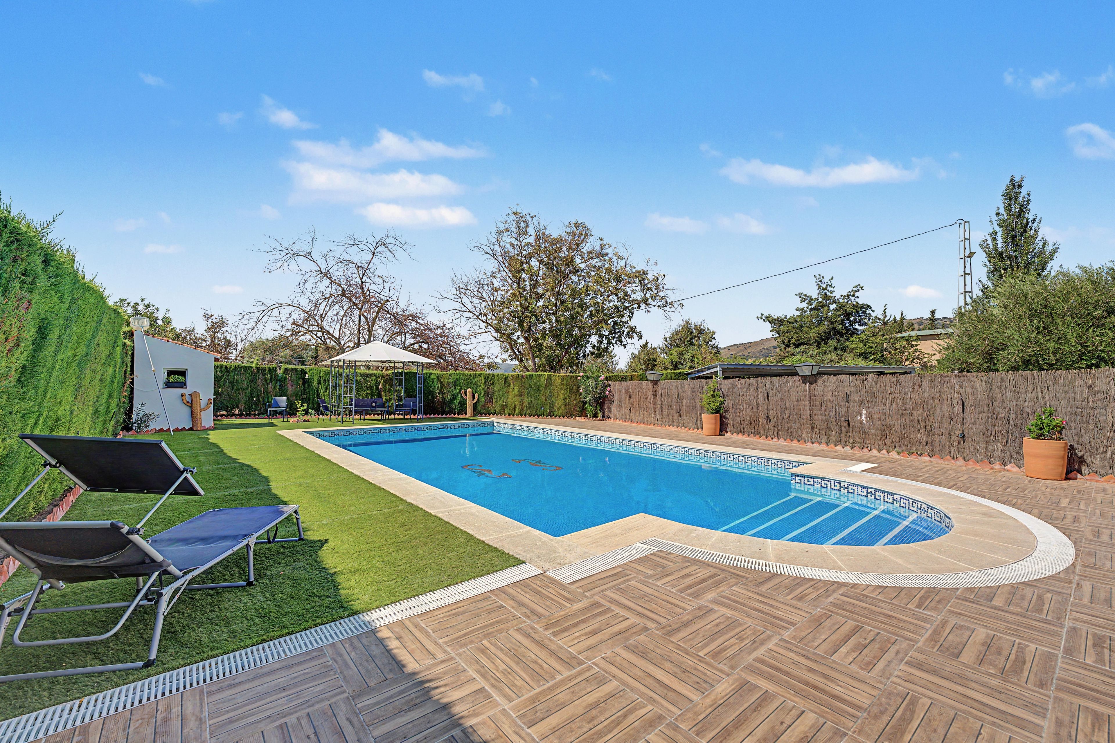 A swimming pool with a herringbone deck pattern, surrounded by a well-maintained lawn and a variety of trees.