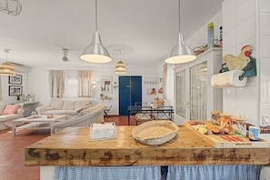 A well-lit living room with a wooden dining table, a sofa, and a kitchen area with a hanging light fixture. - Country House 'Casa La Bruja 1' with Private Pool, Wi-Fi and Air Conditioning (Ronda)