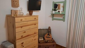 A room with a wooden dresser, a flat-screen TV, a guitar in a wicker box, and a striped curtain.