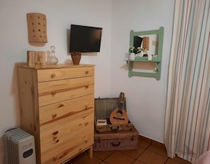 Et værelse med et træskab, et fladskærms-tv, en guitar i en fletkurv og en stribet gardin.