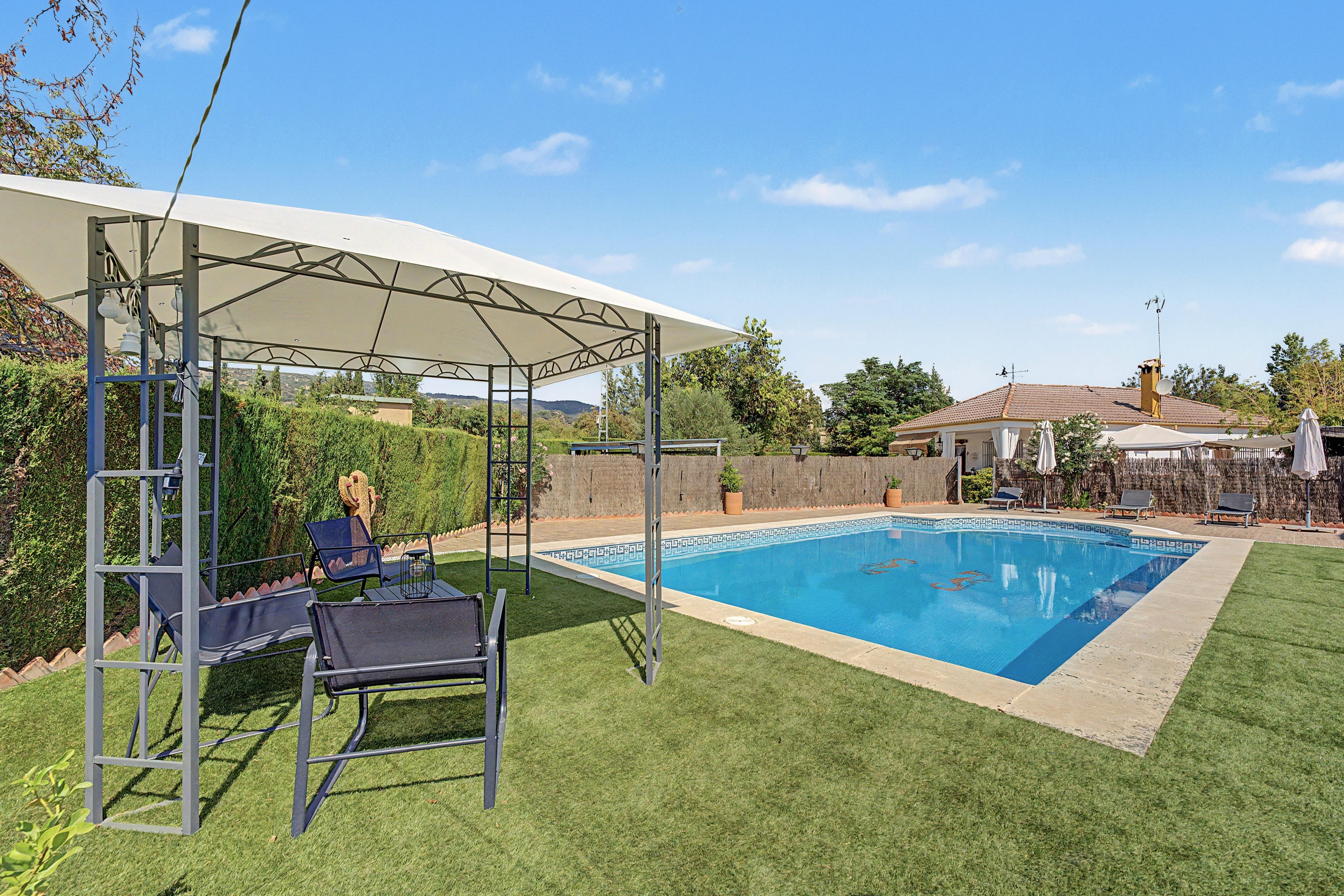 A swimming pool with a covered seating area and lounge chairs.