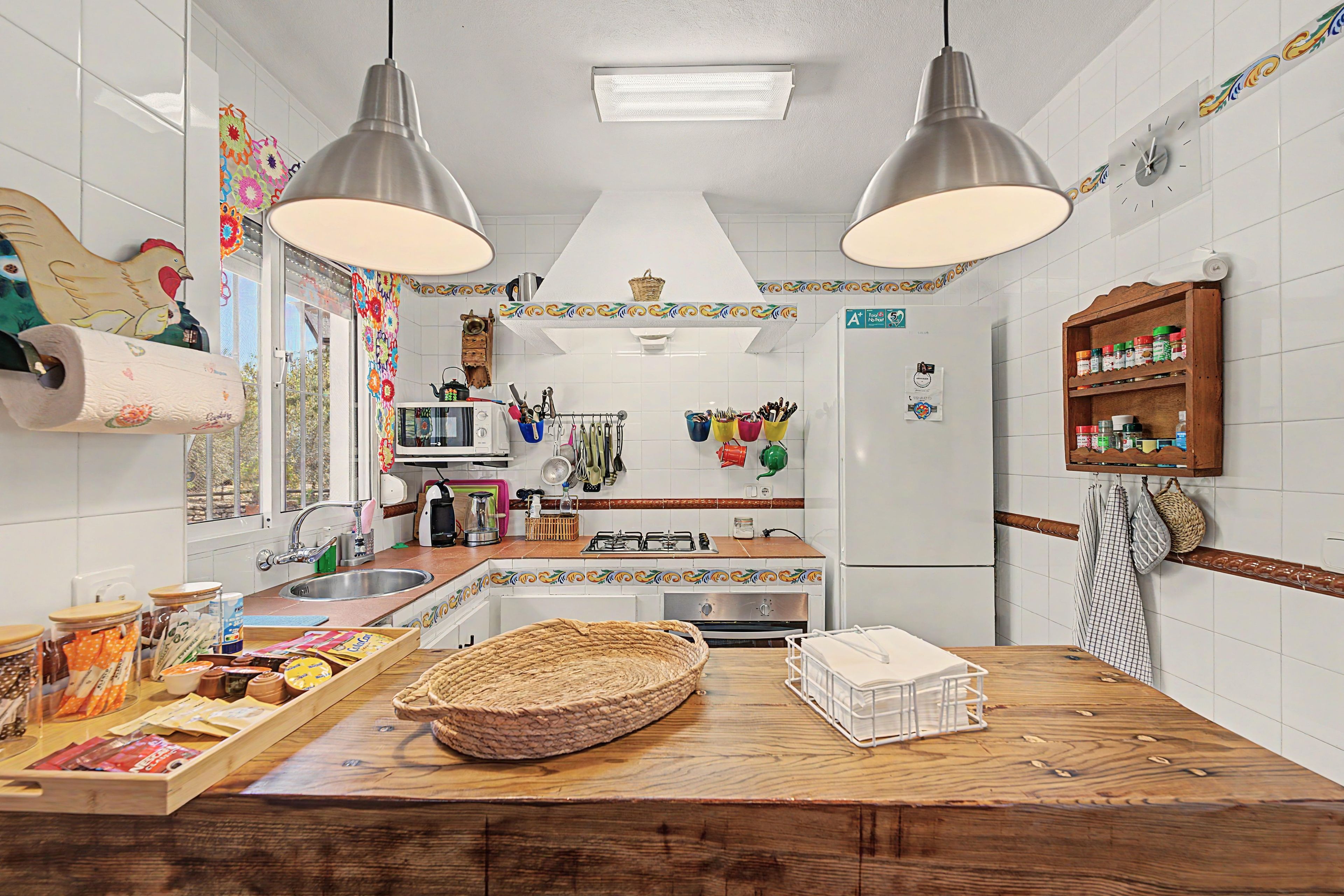 Een keuken met een houten kookeiland, roestvrijstalen apparatuur, hangende keukengerei en een decoratieve spatwand.