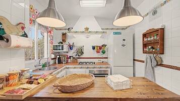 Een keuken met een houten kookeiland, roestvrijstalen apparatuur, hangende keukengerei en een decoratieve spatwand.