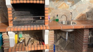 A brick-built outdoor kitchen with a built-in grill, a sink, and a stone wall backdrop.