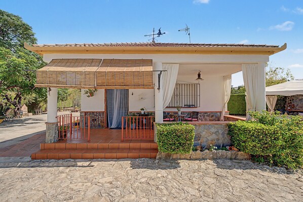 A covered outdoor area with a pergola, seating, and a stone wall.