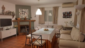 A living room with a fireplace, a dining table with chairs, a sofa, a TV, and a wall-mounted air conditioner.