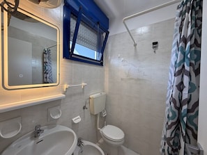 Een badkamer met een wit wastafelmeubel, toilet en douche.