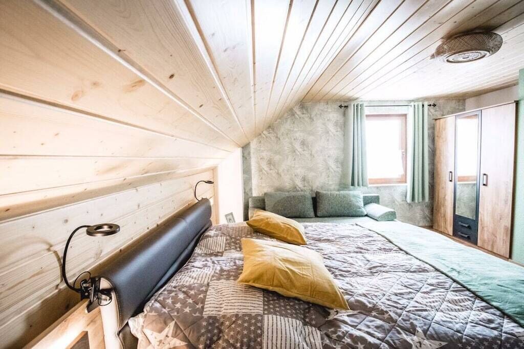 A bedroom with a wooden headboard, a bed with patterned bedding, a window with curtains, and a wardrobe.
