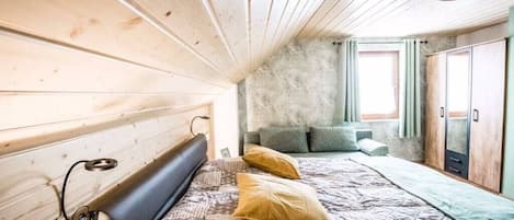 A bedroom with a wooden headboard, a bed with patterned bedding, a window with curtains, and a wardrobe.