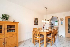 Een eetgedeelte met een houten tafel en stoelen, een kast met glazen deuren en een hangende lamp.