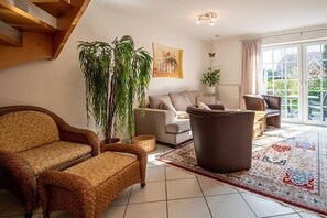 Una sala de estar con sofá, sillón y una planta grande en maceta.
