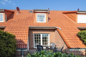 A residential building with a red-tiled roof, a brick exterior, and a small patio with a table and chairs. - FH Luv - Weißner || Hooksiel (Hooksiel)