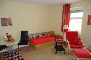 A compact room with a bed, a desk, a chair, and a window with curtains. - Holiday apartment with 1 bedroom (Königstein\/ OT Leupoldishain)