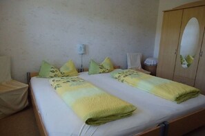 A double bed with a green and yellow blanket, a wooden wardrobe, and a bedside table with a lamp. - Holiday apartment with 1 bedroom (Königstein\/ OT Leupoldishain)