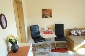 A room with two black chairs, a small white table, a sofa with a floral cushion, a vase with yellow flowers, and a painting on the wall. - Holiday apartment with 1 bedroom (Königstein\/ OT Leupoldishain)