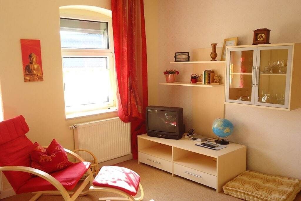 A room with a red chair, a television, a globe, and a cabinet with glass doors.
