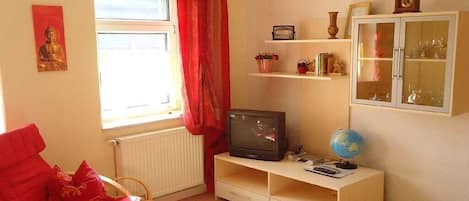 A room with a red chair, a television, a globe, and a cabinet with glass doors.