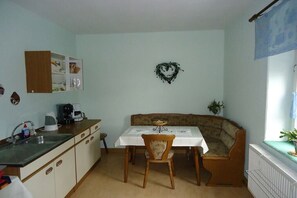 A compact kitchen with a dining table and bench, a small refrigerator, and a heart-shaped decoration on the wall. - Holiday apartment with 1 bedroom (Königstein\/ OT Leupoldishain)
