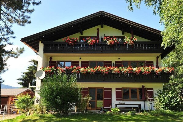 Un immeuble de deux étages doté d’un balcon orné de fleurs, d’une antenne parabolique et d’un banc situé dans le jardin avant.