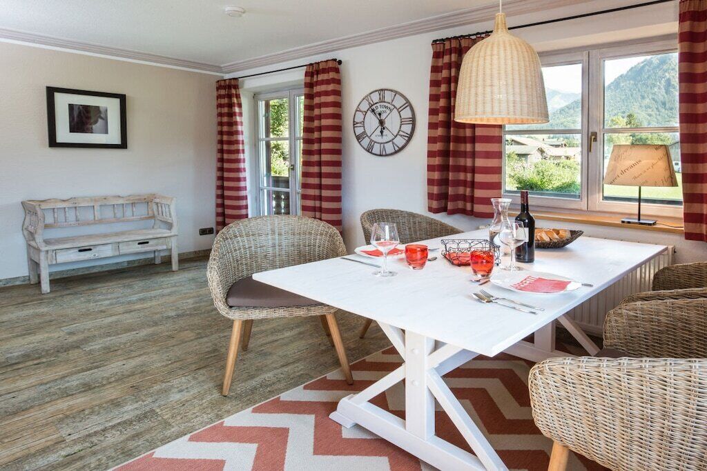 A dining area with wicker chairs, a white table, and a clock on the wall.