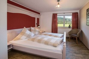 Une chambre à coucher avec un lit, une chaise, une fenêtre avec des rideaux et un mur orné d’une affiche.