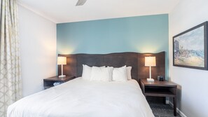 A hotel room with a large bed, two bedside tables with lamps, a headboard, and a painting on the wall. - North Myrtle Beach | Ocean Breeze Stay | Pool & Beach | 2BR (North Myrtle Beach)