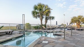 A swimming pool with lounge chairs, palm trees, and a view of the ocean. - North Myrtle Beach | Ocean Breeze Stay | Pool & Beach | 2BR (North Myrtle Beach)