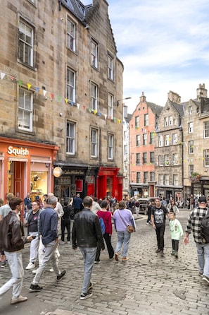 Eine Kopfsteinpflasterstraße mit historischen Gebäuden, einem sichtbaren Geschäft namens 'Squish' und einer Menschenmenge.