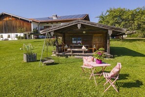 A wooden cabin with a porch, a table with chairs, and a small garden area. - Lavender - Sotterhof (Inzell)