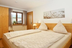 A bedroom with a double bed, a wooden wardrobe, a window with curtains, a wall-mounted lamp, and a painting. - Lavender - Sotterhof (Inzell)