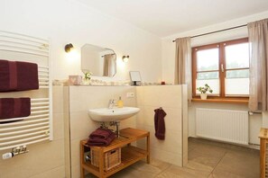 A bathroom with a white sink, mirror, and towel rack. There is a window with curtains and a plant on the windowsill. - Lavender - Sotterhof (Inzell)