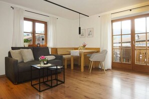 A furnished living room with a sofa, a coffee table, a dining table with chairs, and large windows with curtains. - Lavender - Sotterhof (Inzell)