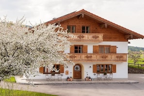 A two-story wooden house with a balcony, a front door, and a small outdoor seating area. - Lavender - Sotterhof (Inzell)