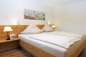 A bedroom with a wooden headboard, two bedside lamps, a bedside table with a book, and a wall-mounted picture. - Lavender - Sotterhof (Inzell)