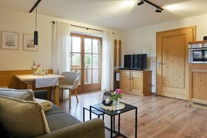 A cozy living area with a sofa, a small table with a vase, a television, and wooden cabinets. - Lavender - Sotterhof (Inzell)